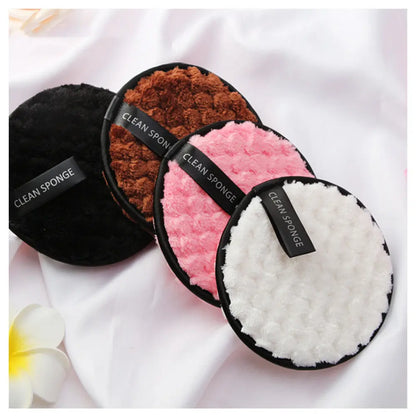 Four round soft clean sponges in black, brown, pink, and white colors on white fabric