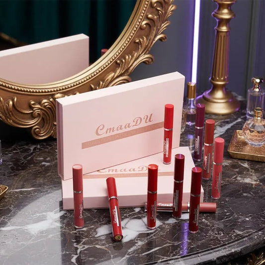 Collection of CmaaDu lipsticks on a marble surface with a decorative mirror and lamp in the background.
