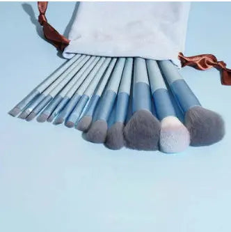 Set of blue makeup brushes with gray bristles in a white pouch on light blue background