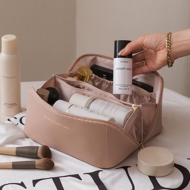 Cosmetic bag with skincare products and makeup brushes on a table.