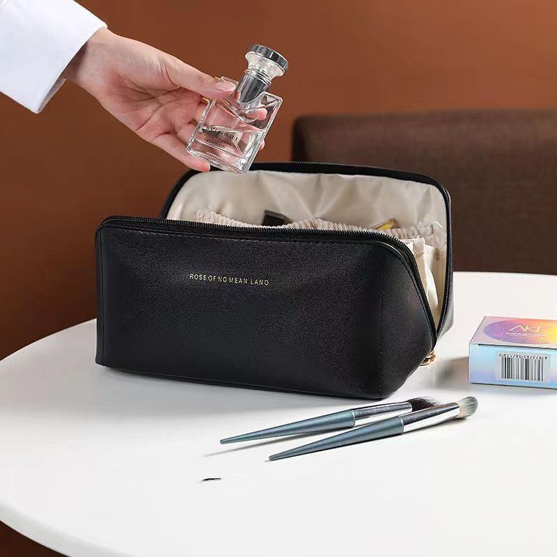 Black cosmetic bag with makeup brushes and a small bottle on a white surface.
