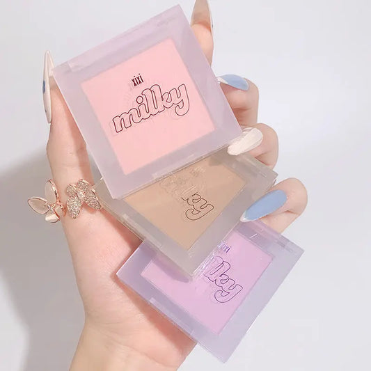 Hand holding a compact powder with 'milky' branding on a light background