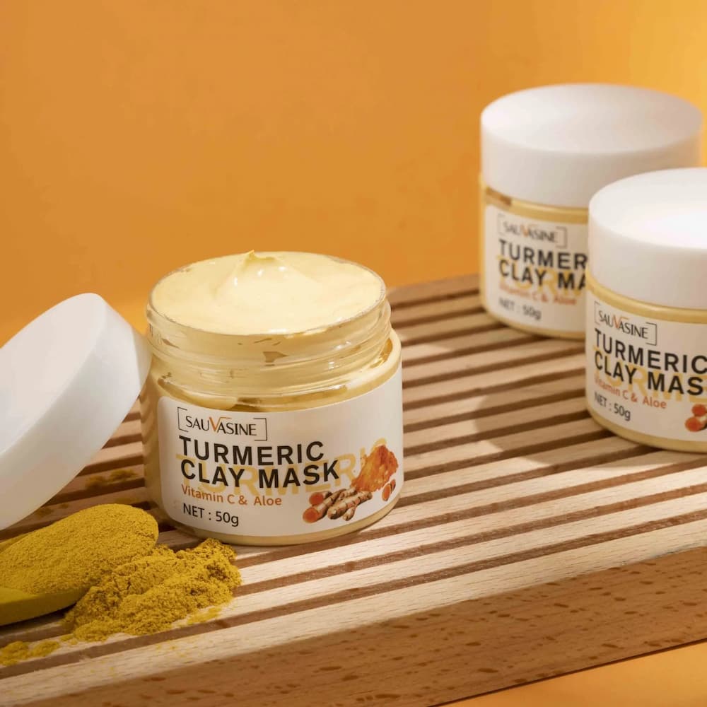 Jar of Sauvasine Turmeric Clay Mask on a wooden surface with turmeric powder.