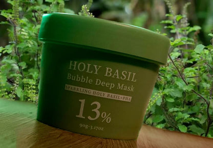 Green container of Holy Basil Bubble Deep Mask with basil plants in the background